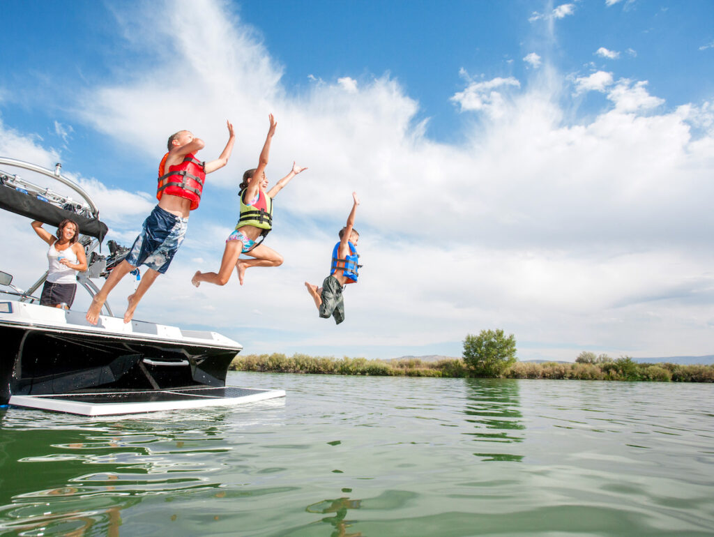Kids jumping off the back of a boat into the water.