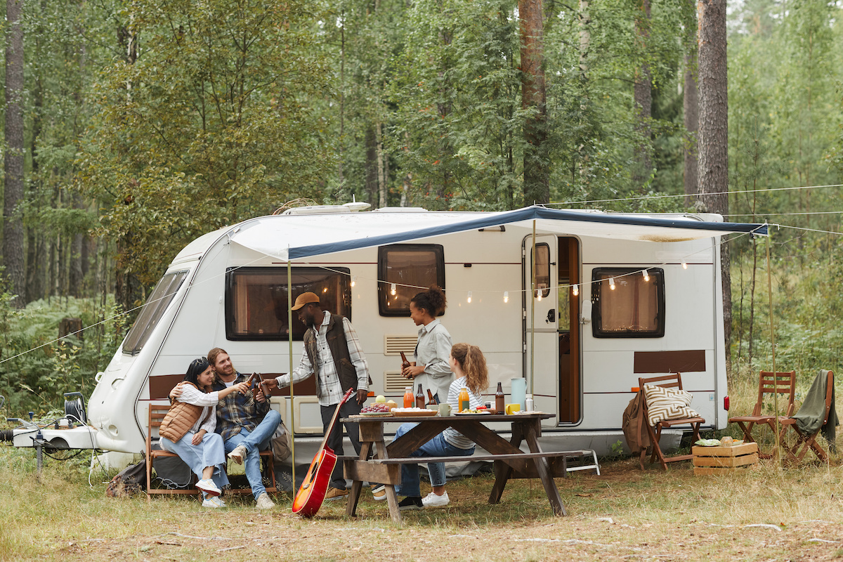 Wide angle view of young people enjoying outdoors while camping with van in forest.