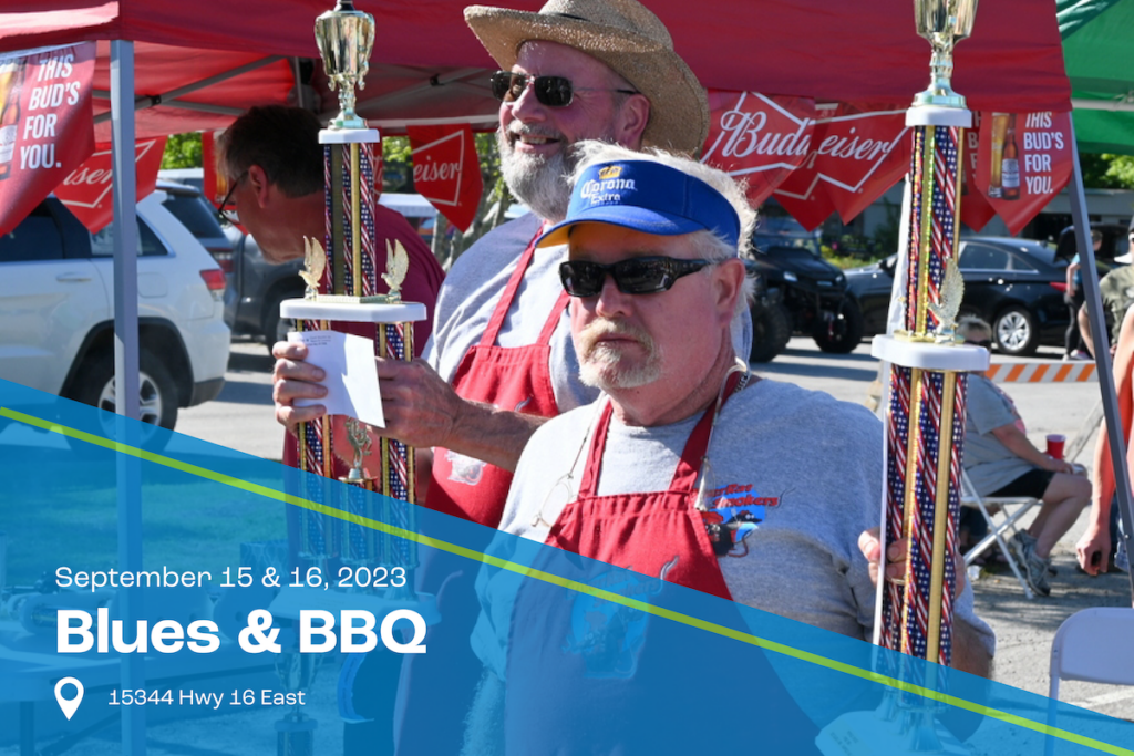 Winner of BBQ contest wearing red aprons and holding up 1st place trophies.