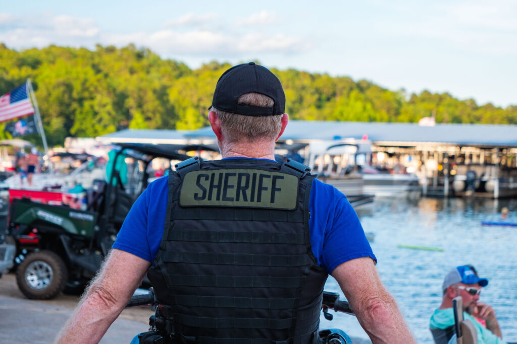 A man in a vest with "Sheriff" on the back oversees the security of the event.