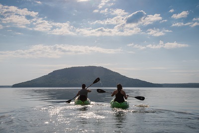 A couple kayaking on Greers Ferry Lake, toward Sugar Loaf Mountain.