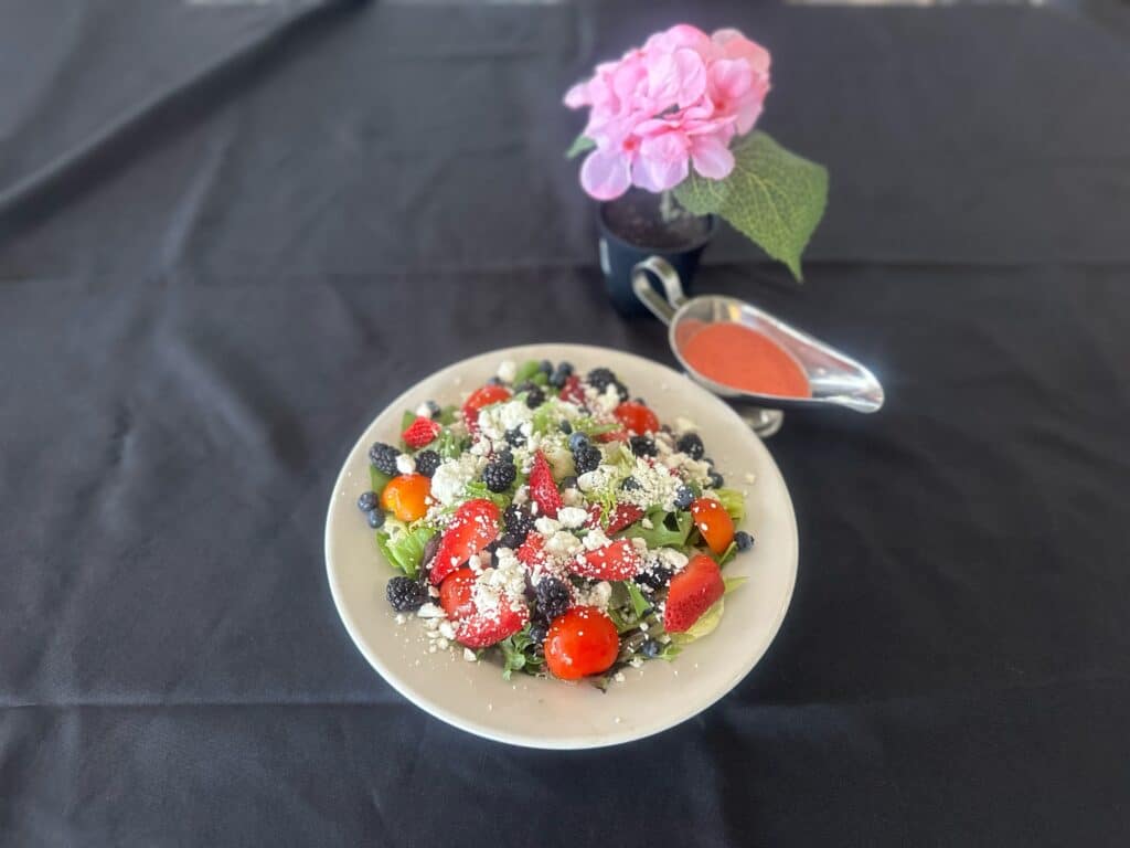 A salad from Little Red Restaurant that consists of lettuce, strawberries, blueberries, blackberries, cherry tomatoes, and feta cheese. Served with a vinaigrette dressing.